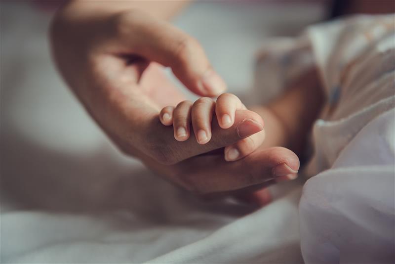 Tiny baby hand holding adult hand finger as a representation of pioneering better maternal health